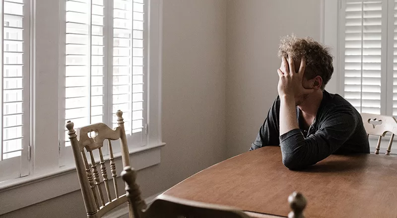 Man sat at a dining table holding his head in his hands