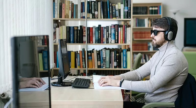 Man wearing headphones reading a braille book