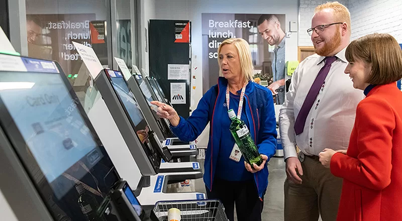 Tesco sales assistant helping with self service till